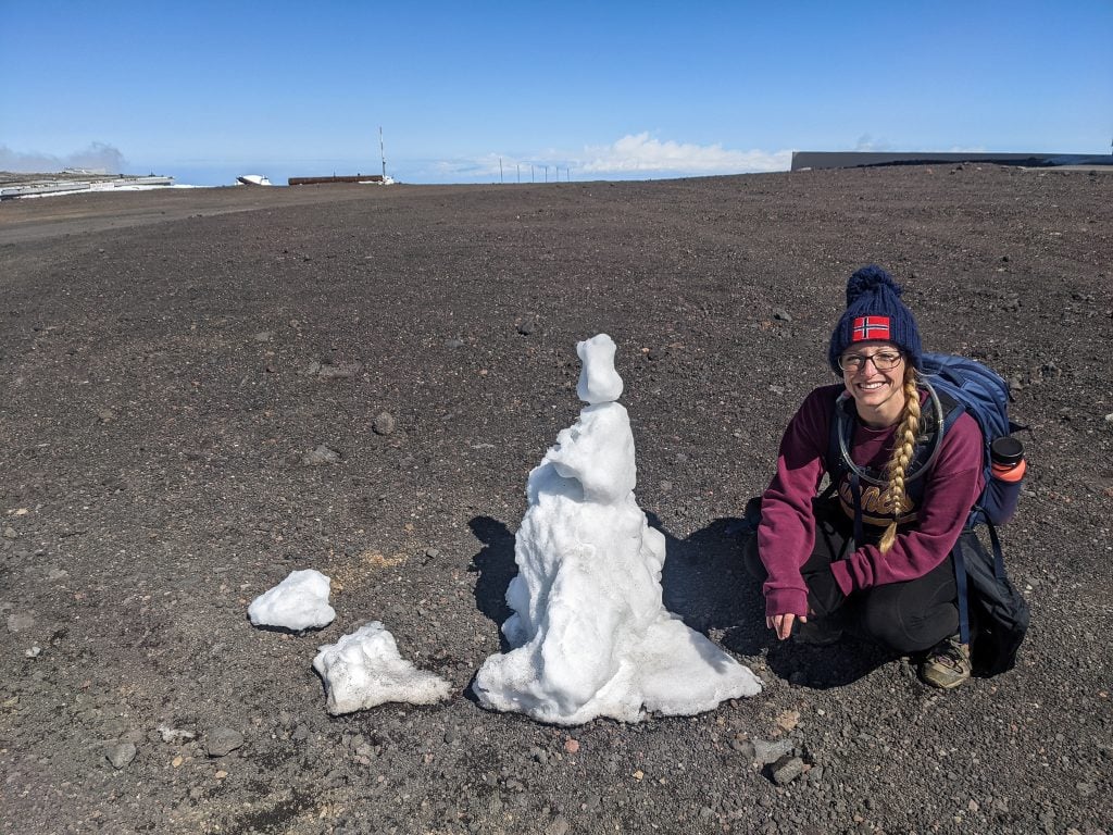 Laura Sitting Next To A Snowman At The Top of Mauna Kea.
